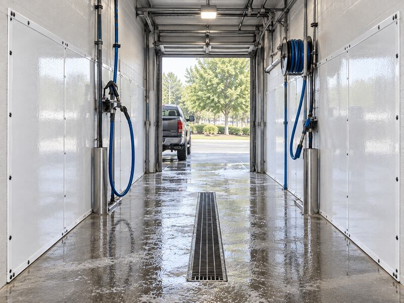 Truck exiting a wash bay tunnel lined with car wash wall panels and hose reels
