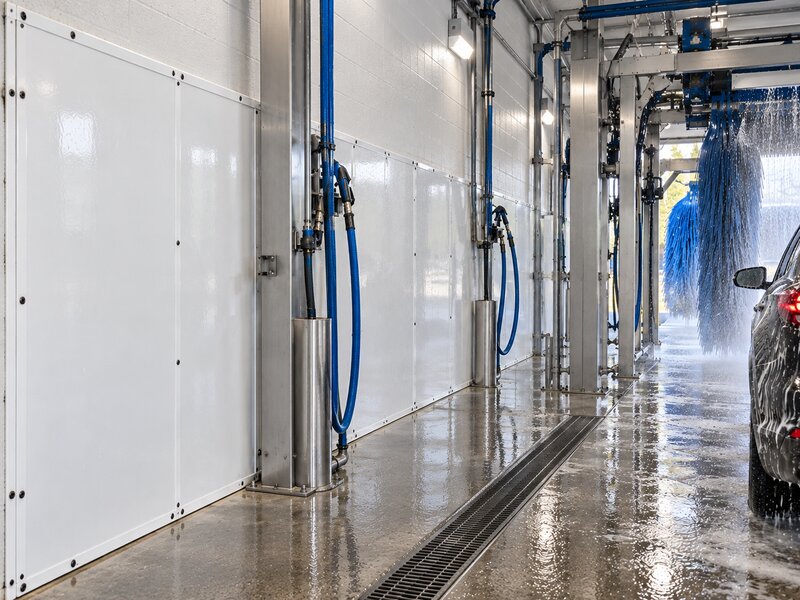 Car wash wall panels lining a tunnel bay with multiple hose stations and brush equipment
