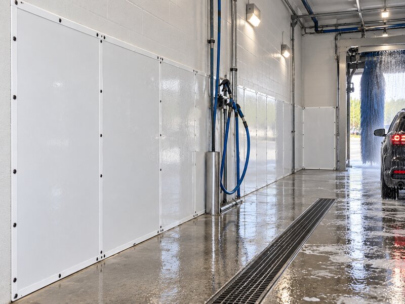 White HDPE car wash wall panels installed along a wash bay wall with hose reel and brush tunnel visible
