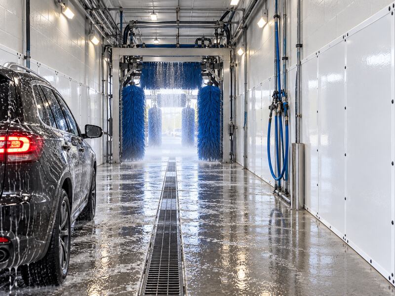 Vehicle passing through an automated brush wash tunnel lined with white HDPE wall panels
