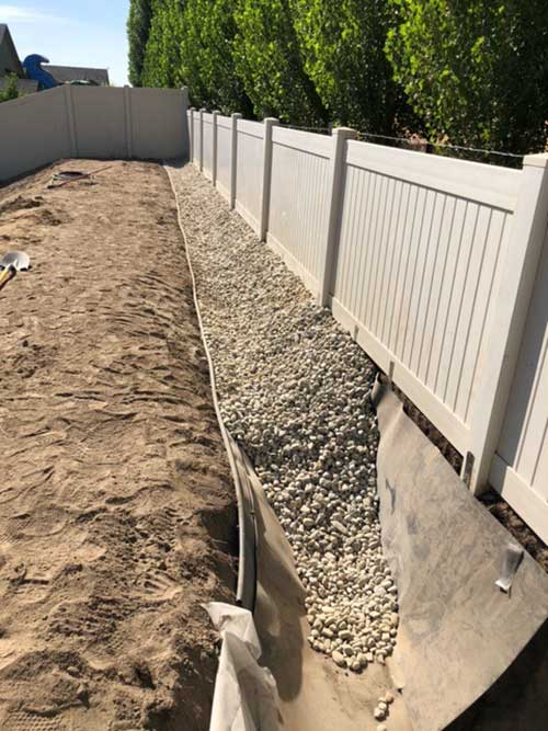 Drainage ditch liner installed and filled with drain rock.