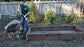 Man shoveling soil into wheelbarrow next to raised garden bed lined with gopher wire mesh
