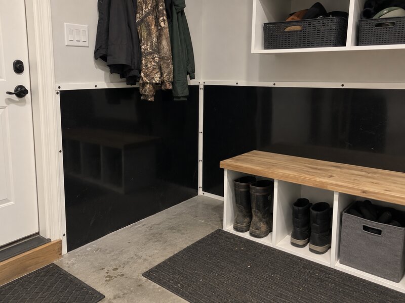 Mudroom entry with black HDPE wall liner installed behind a boot bench and coat hooks
