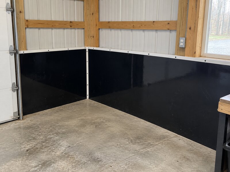 Pole barn interior corner with black HDPE wall liner installed along the base of metal walls
