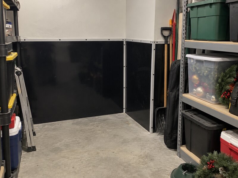 Garage storage corner with black HDPE wall liner behind metal shelving and storage bins
