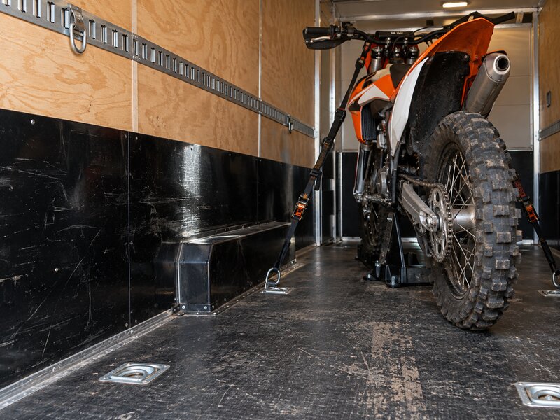 Dirt bike strapped down inside a cargo trailer lined with black HDPE wall panels
