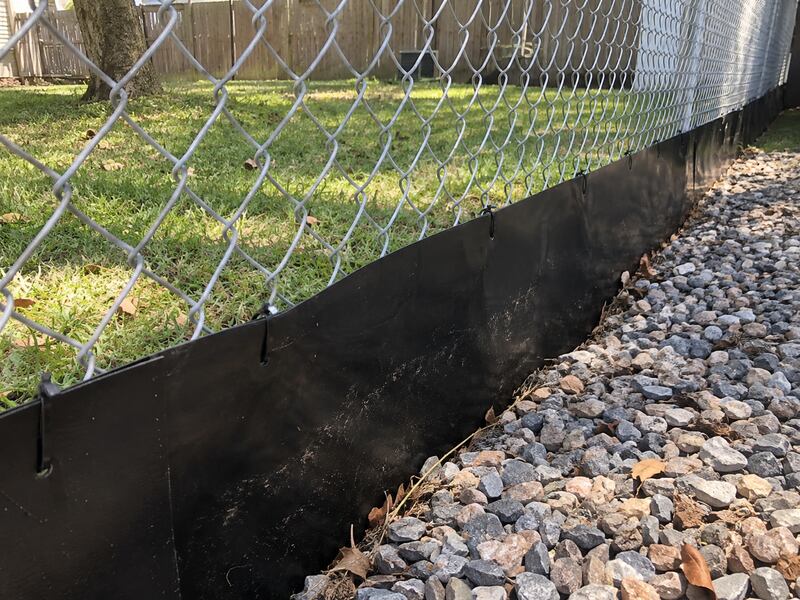 HDPE fence barrier installed along a chain link fence over gravel landscaping
