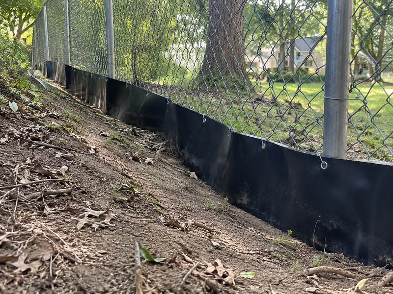 Black HDPE under fence barrier along a chain link fence on a sloped hillside
