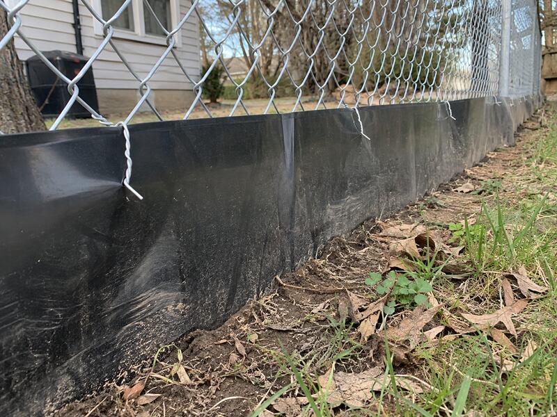 Black HDPE bottom barrier installed along a chain link fence beside a house
