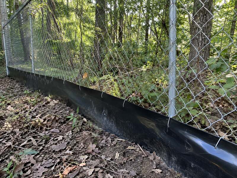 HDPE dig barrier along a chain link fence running through a wooded area
