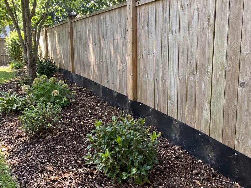 HDPE under fence barrier along a wood privacy fence bordering a mulched garden bed
