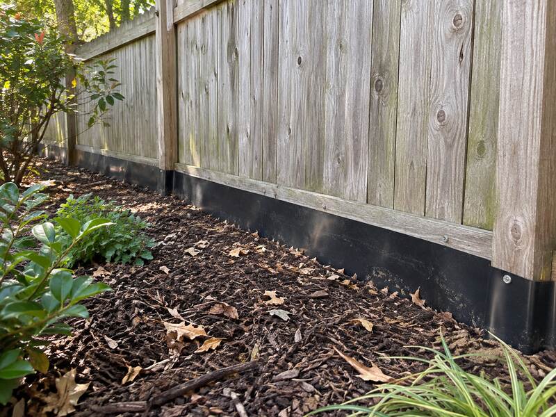 HDPE under fence barrier along a wood fence bordering a mulched shrub bed
