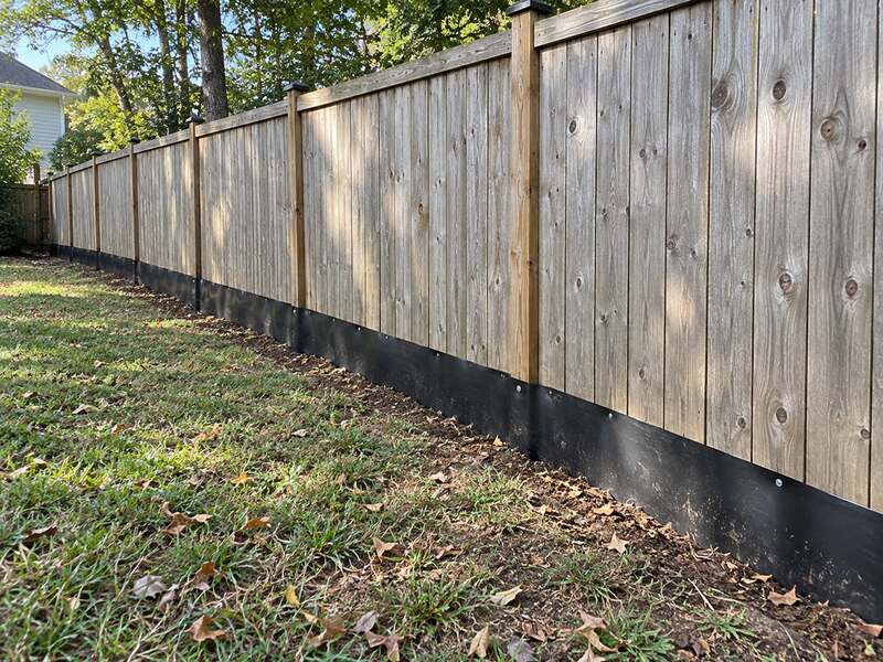 HDPE under fence barrier following a curved wood privacy fence line across a grass yard
