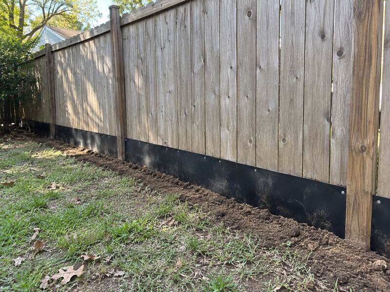 Long straight run of black HDPE under fence barrier along a wood privacy fence
