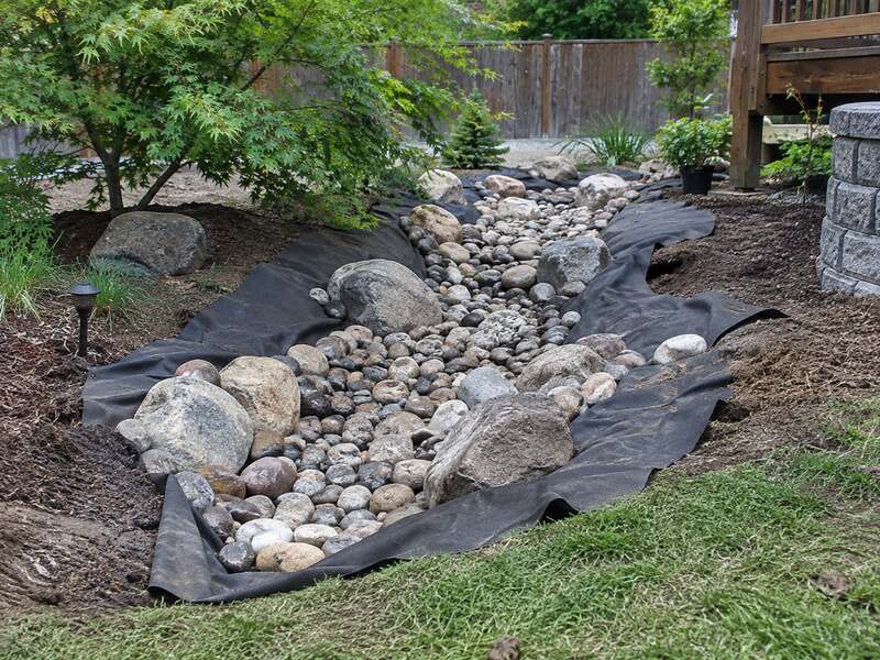 Non-woven fabric lining a dry creek bed rock channel with boulders in a backyard landscape

