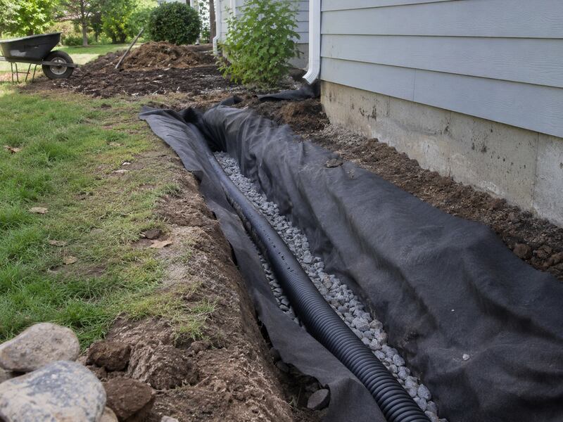 Non-woven fabric wrapping gravel and drain pipe along a house foundation trench

