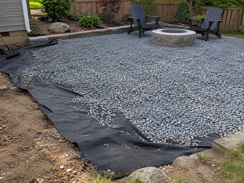 Non-woven fabric lining a gravel patio installation around a stone fire pit
