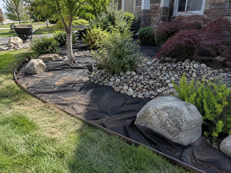 Non-woven fabric lining a tree ring and river rock planting bed in a front yard
