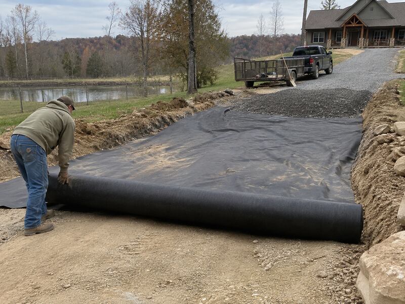 Non-woven geotextile fabric being rolled out over a gravel driveway base
