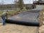 Non-woven geotextile fabric being rolled out over a gravel driveway base
