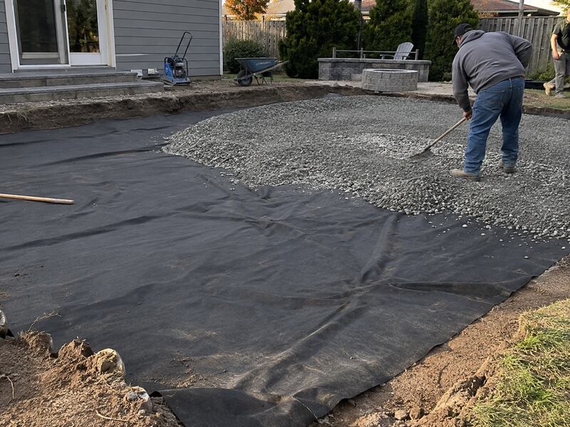 Non-woven geotextile fabric laid under gravel for a backyard patio base installation
