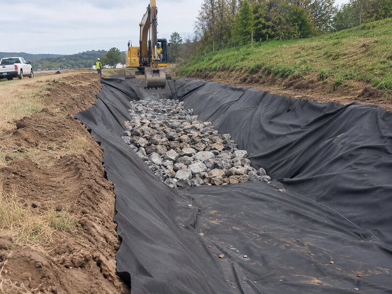 Non-woven geotextile fabric lining a roadside drainage ditch filled with rock
