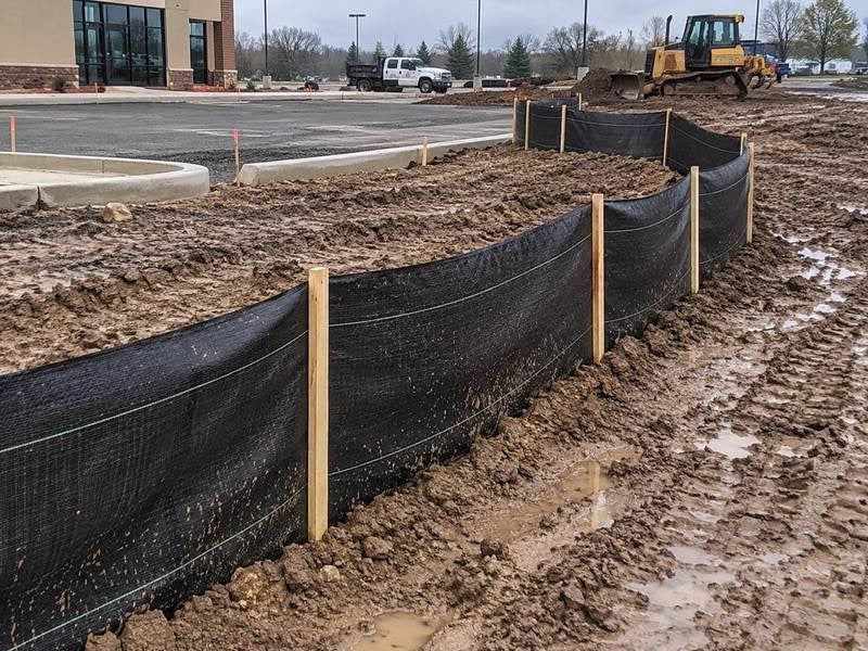 Silt fence installed around a muddy commercial parking lot construction site
