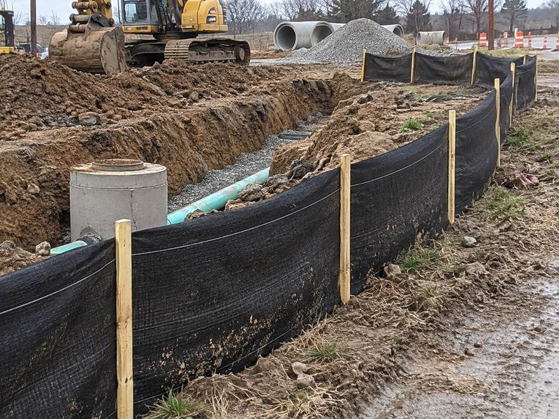 Silt fence installed beside a utility trench with pipe at a construction site
