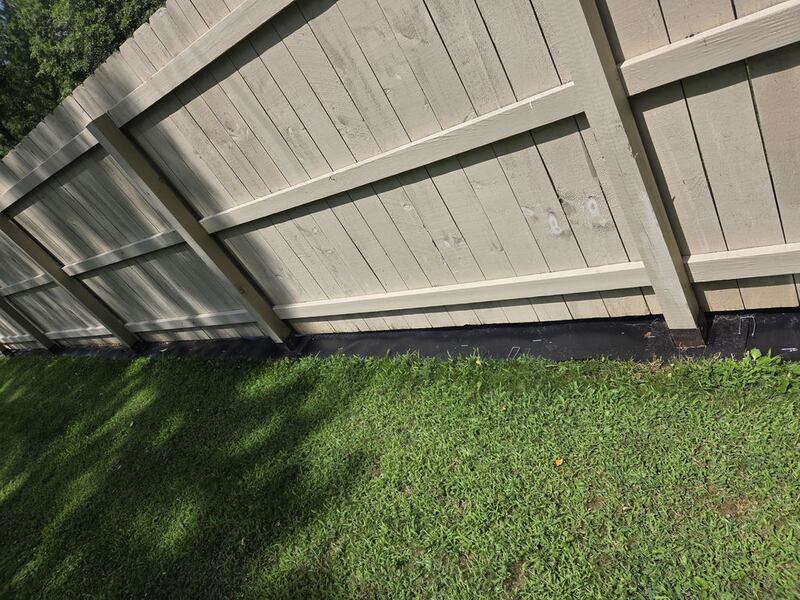 Black under-fence plastic barrier installed along the bottom of a wood privacy fence

